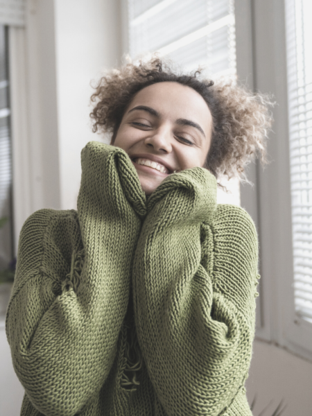 A woman in a cozy sweater smiling and practicing self love.