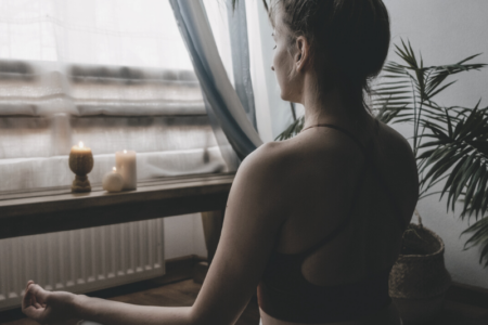 A woman practicing spiritual meditation sitting by the window with candles lit.