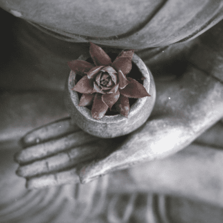 A Buddhist statue of Buddha holding a flower while sitting in lotus position.