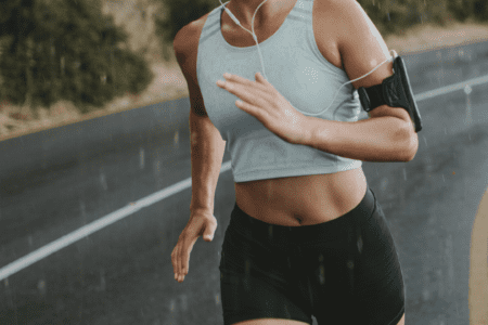 A Blonde woman jogging down a windy road with headphones in her ears.