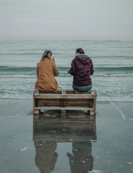 Two people chatting on a bench alongside the ocean